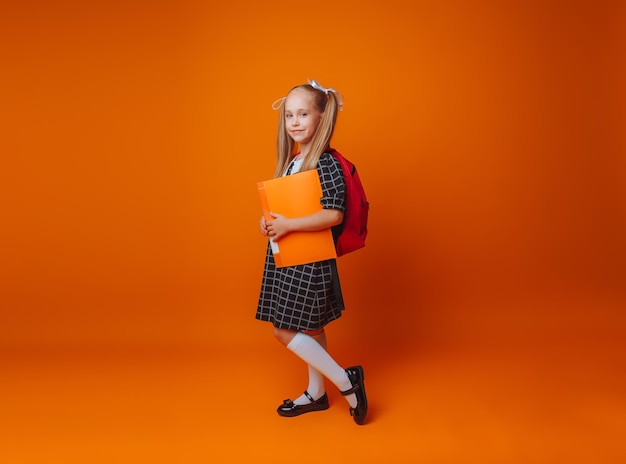 Regreso a la escuela Una colegiala con una mochila escolar sobre un fondo de estudio amarillo aislado una niña sostiene una carpeta y una mochila