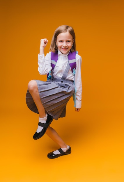 Regreso a la escuela Una colegiala sostiene libros en sus manos una niña sobre un fondo de estudio amarillo aislado Corre y salta saltando bebé de regreso a la escuela