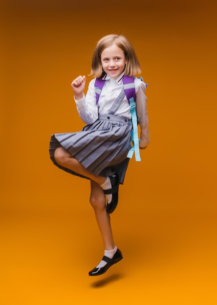 Regreso a la escuela Una colegiala sostiene libros en sus manos una niña sobre un fondo de estudio amarillo aislado Corre y salta saltando bebé de regreso a la escuela