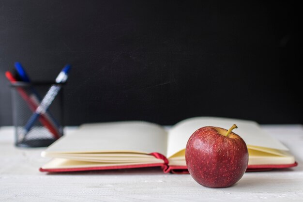 Regreso a la escuela, concepto de educación y conocimiento, manzana y cuaderno en la mesa frente a la pizarra