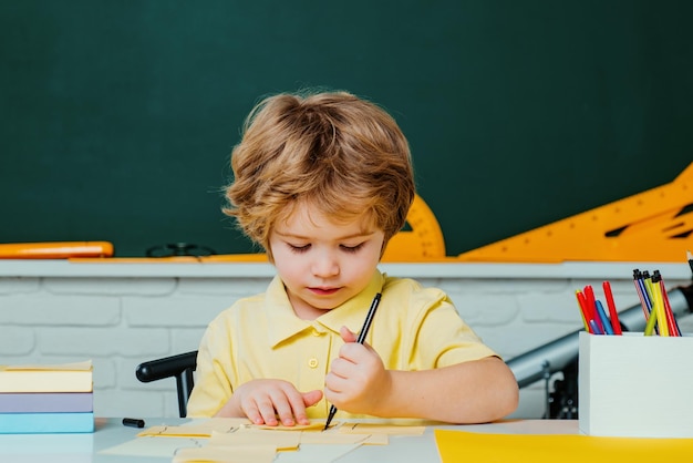 Regreso a la escuela Feliz alumno sonriente dibujando en el escritorio Lindo niño preescolar con maestro st