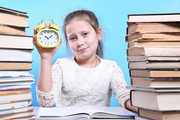 Regreso a la escuela. Feliz niño trabajador lindo está sentado en un escritorio en el interior. Kid está aprendiendo en clase aprendiendo en casa. Montones de libros a los lados