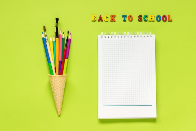 Regreso a la escuela y lápices de colores pincel en cono de helado de galleta y cuaderno sobre fondo verde.