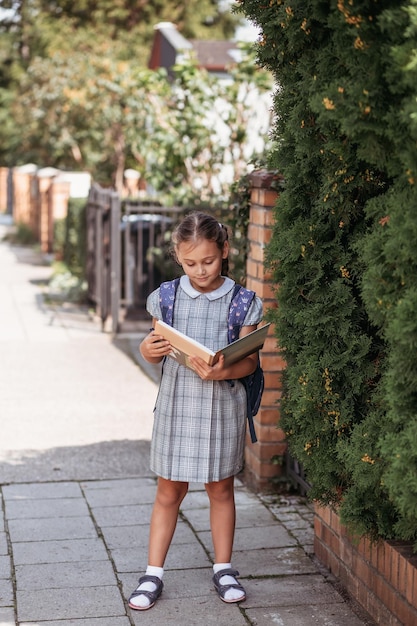 Regreso a la escuela Una linda colegiala con un vestido con coletas y grandes mochilas azules sostiene libros y camina en el patio de la escuela Una niña va al primer grado