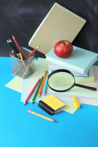 Foto regreso a la escuela, pila de libros, lupa y papelería en la mesa