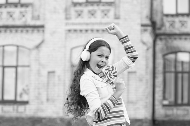 Regreso a la escuela vocal belleza feliz niño al aire libre educación innovadora feliz día del niño estilo de vida saludable colegiala con piruleta niño feliz en auricular alumno escuchar música y cantar canción