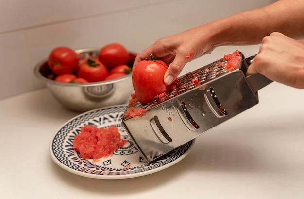 Reiben von Tomaten durch eine Metallreibe in der Küche