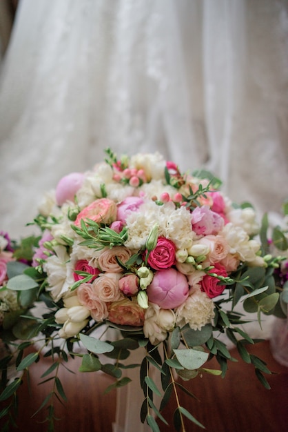 Reicher rosa Hochzeitsblumenstrauß steht auf dem Boden vor einem Hochzeitskleid