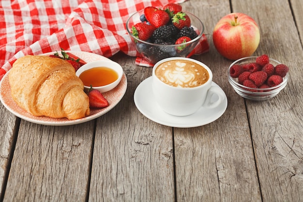 Reichhaltiges kontinentales Frühstück. Knusprige französische Croissants, Kaffee, Honig und viele süße Beeren für leckere Morgenmahlzeiten. Köstlicher Start in den Tag, Kopierraum