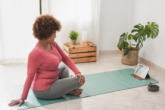 Reife afrikanische Frau, die zu Hause Yoga-Übungen mit einem digitalen Tablet macht