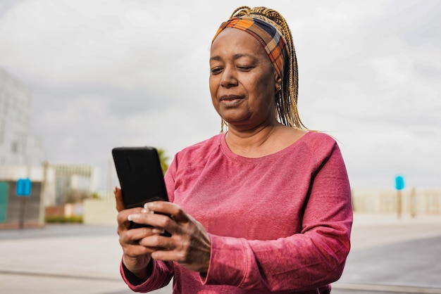 Reife afrikanische Frau mit Handy nach dem Sporttraining in der Stadt