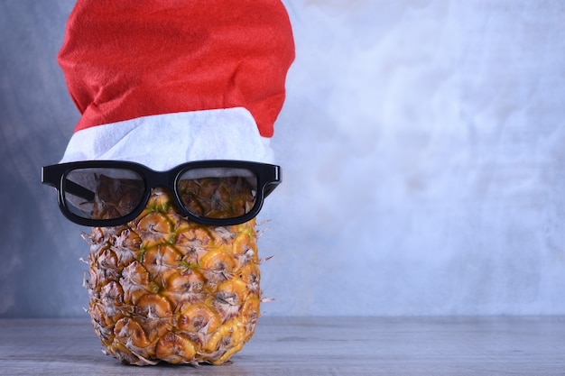 Reife Ananas, Ananas mit Sonnenbrille in Weihnachtsmütze. Neujahrsfruchtkonzept