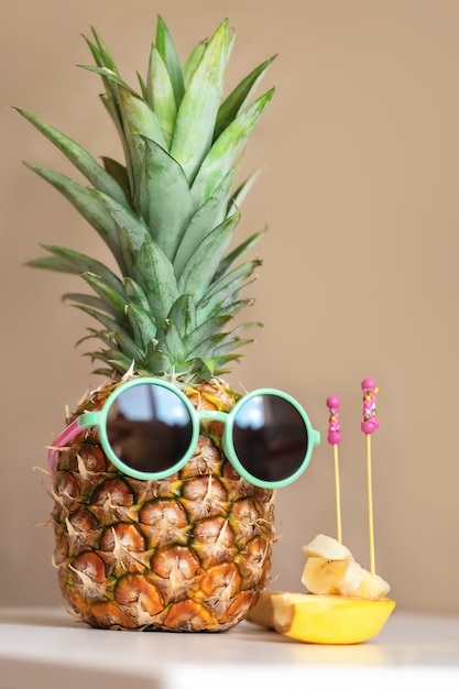 Foto reife ananas mit sonnenbrille steht auf dem tisch an einer beigen wand