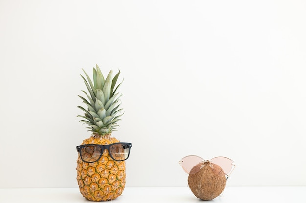 Reife Ananas und Kokosnuss in Sonnenbrillen auf weißem Hintergrund Sommerurlaub Hallo Sommer
