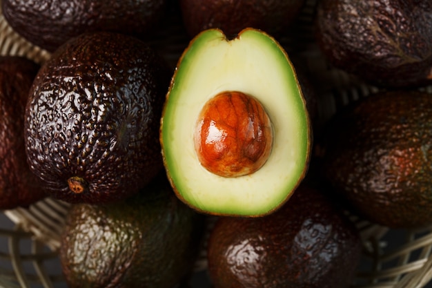 Reife Avocados in einem Korb auf einem schwarzen Tisch, mit einer geschnittenen Frucht und einem Stein. Makro, Nahaufnahme