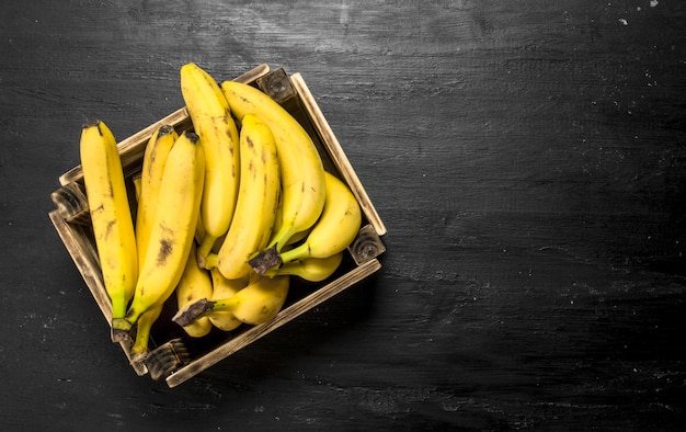 Reife Bananen in einer alten Schachtel auf schwarzer Tafel.