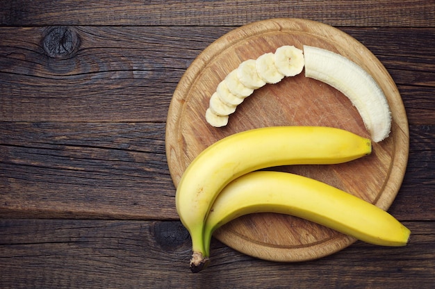 Reife Bananen und ein Aufschnitt auf Holzbrett, Ansicht von oben