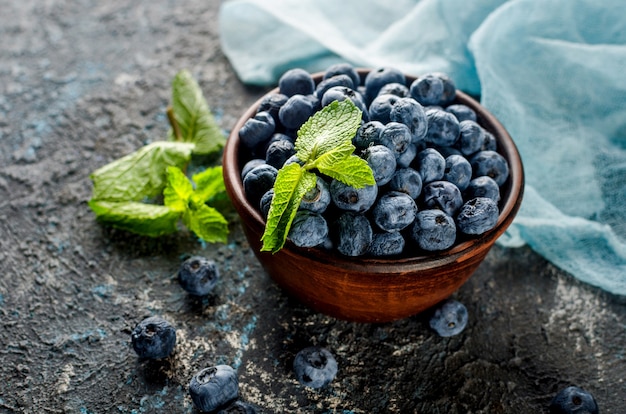 Reife Blaubeeren in der Keramikschale mit Blattminze auf dunklem Hintergrund