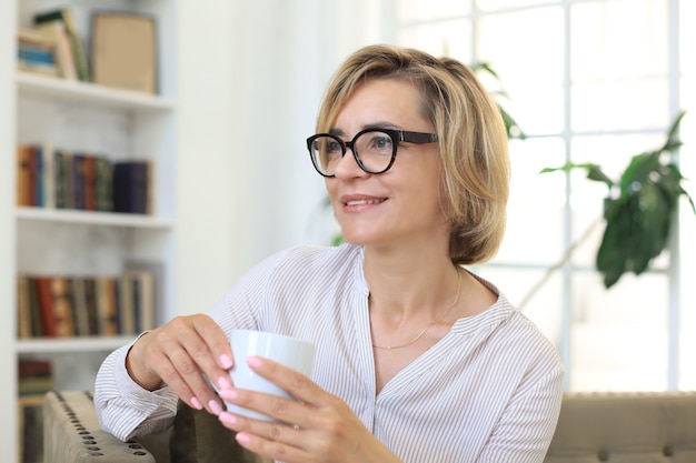 Reife blonde Frau in der Couch mit einem Tee oder Kaffee.