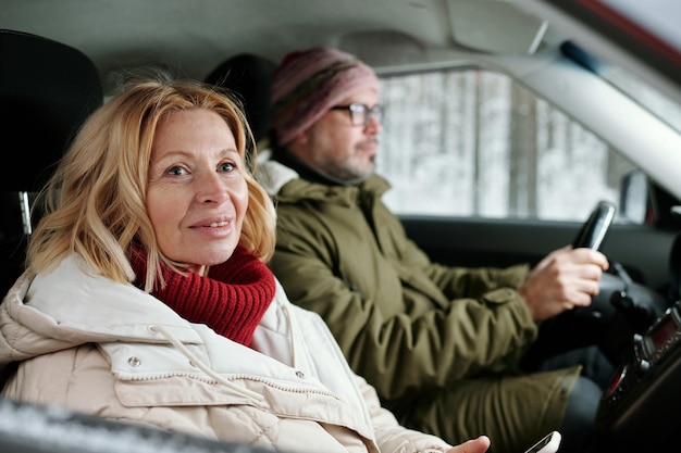 Reife blonde Frau in warmem Strickpullover und weißer Winterjacke