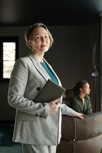 Reife blonde Psychotherapeutin mit Notizbuch in der Hand und Blick in die Kamera