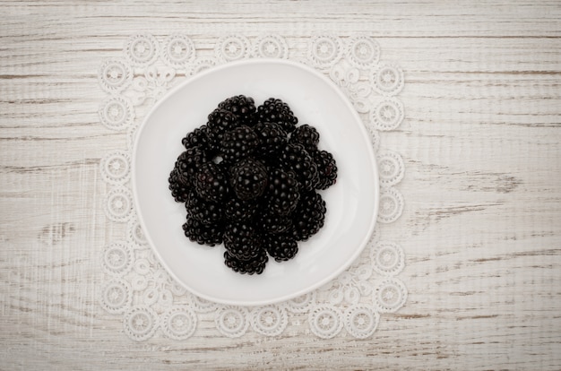 Reife Brombeeren auf einer weißen Untertasse. weißer Holztisch, Draufsicht