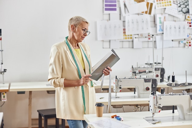 Reife Dame betrachtet offenen Ordner, der Nera-Arbeitsplatz mit Nähmaschine steht