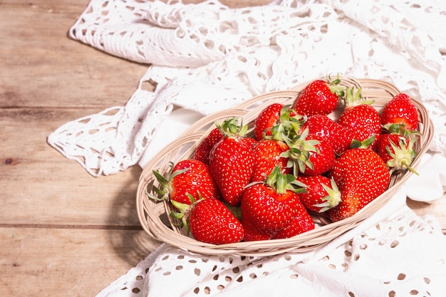 Reife Erdbeeren im Korbteller. Frische Beeren, aromatische Minze. Alter Holztisch, Vintage gehäkelte Serviette, rustikaler Stil, Kopierraum