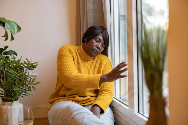 Reife Frau Depression nach Hause traurige afroamerikanische ältere Frau, die aus dem Fenster schaut