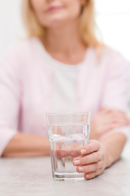 Reife frau der nahaufnahme, die ein glas wasser hält