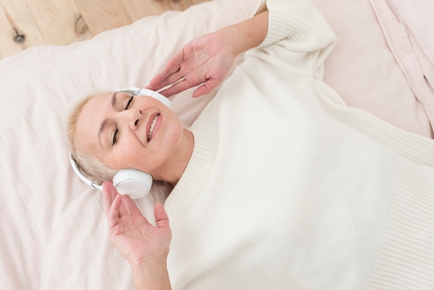 Foto reife frau des smiley, die musik auf kopfhörern im bett genießt