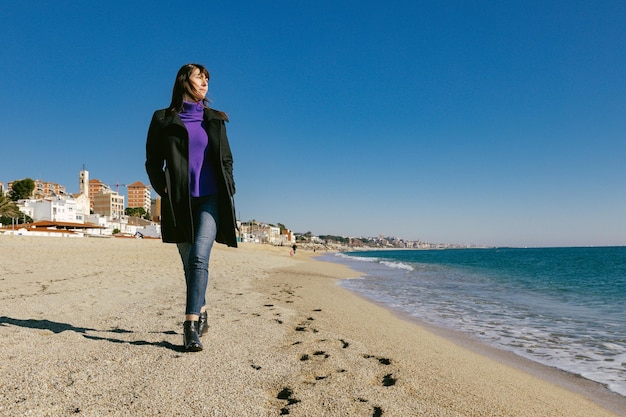 Reife Frau, die an einem sonnigen Wintertag am Strand spazieren geht