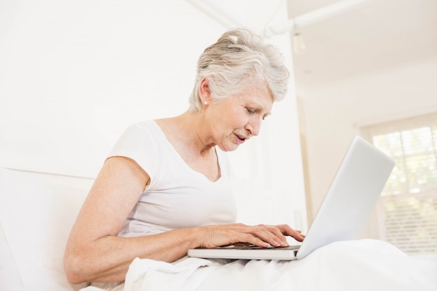 Reife Frau, die den Laptop sitzt auf Bett verwendet