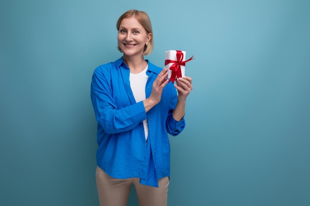 Reife Frau, die Geschenk für Feiertag auf blauem Hintergrundkopienraum gibt