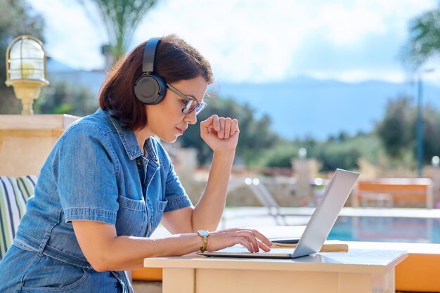 Reife Frau, die im Freien mit Kopfhörern mit Laptop arbeitet
