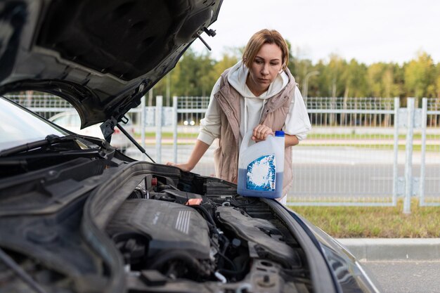 Reife Frau gießt Kühlmittel in den Motor eines kaputten Autos