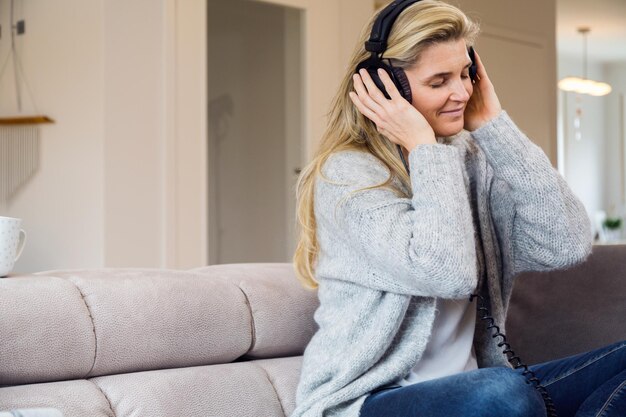 Foto reife frau hört musik mit kopfhörern, während sie sich zu hause ausruht