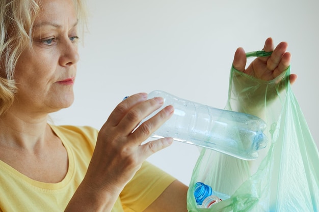 Foto reife frau im gelben t-shirt, die eine leere plastikflasche in einen müllsack steckt