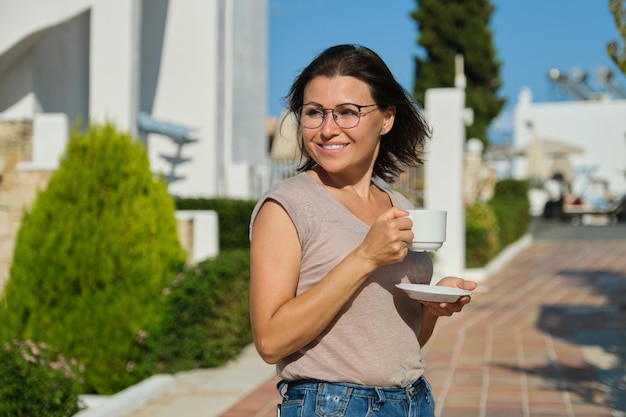 Reife Frau in Gläsern mit Tasse Kaffee zu Fuß im Freien, Porträt einer lächelnden Frau mittleren Alters