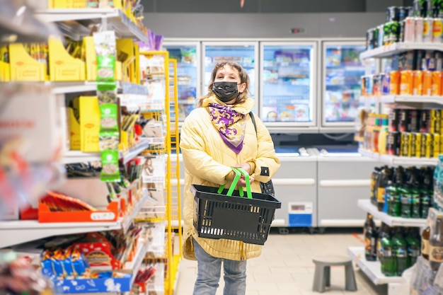 Reife Frau in Schutzmaske, die Lebensmittel in Regalen im Lebensmittelgeschäft auswählt