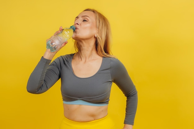 Reife Frau in Sportbekleidung mit einer Flasche Wasser auf gelbem Hintergrund