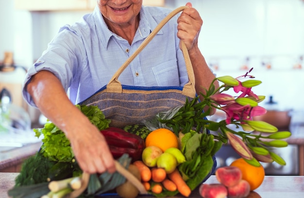 Reife Frau kommt aus dem Lebensmittelgeschäft und legt ihre Einkaufstasche auf den Tisch voller Gemüse und Obst für einen gesunden Essstil Inflations- und Preiserhöhungskonzept