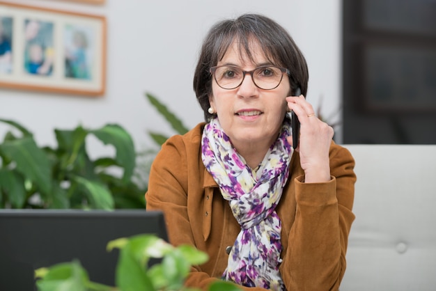 Reife Frau mit brauner Jacke zu Hause sprechend am Telefon