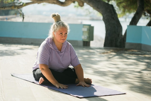 Reife Frau mit Dreadlocks, die Yoga-Übungen am Strand macht, Wellness-Wohlbefinden und aktives älteres Alterskonzept