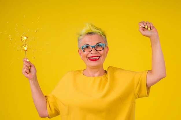 Reife Frau mit farbigen, stilvollen, gelb gefärbten Haaren in warmem Kleid mit leicht funkelndem Hintergrund Studio Copy Spase.