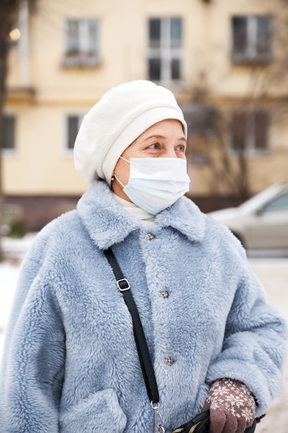Reife Frau mit Gesichtsmaskenschutz, ältere Frau in Gesichtsmaske wegen Luftverschmutzung in der Abendstadt, kranke alte Leute mit medizinischer Maske. Verschmutzung, Stauballergie und Gesundheitskonzept