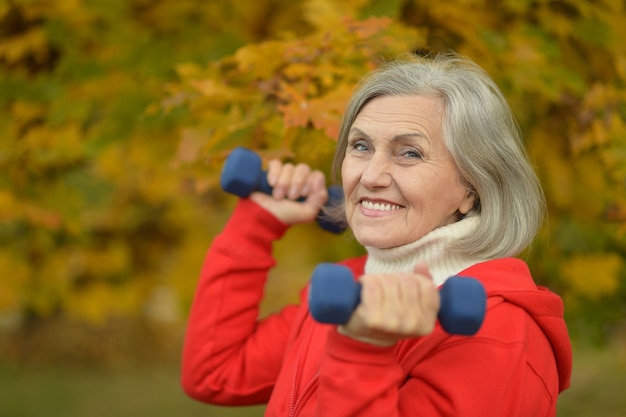 Reife Frau mit Hanteln im Herbstpark