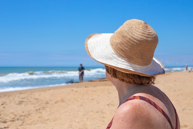 Reife Frau mit Hut am Sandstrand blickt auf das Meer Seitenansicht Rest der Rentner in Russland