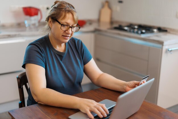 Reife Frau mit Kreditkarte, die zu Hause online bezahlt