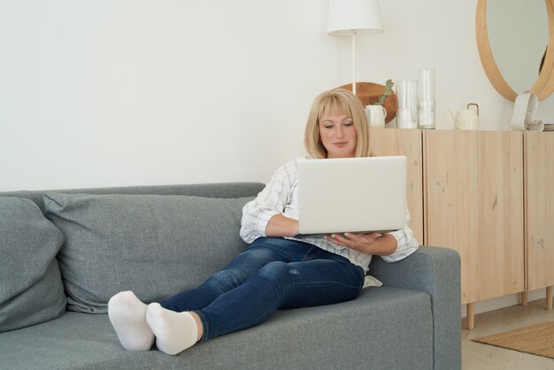 Reife Frau mit Laptop beim Sitzen auf bequemem Sofa